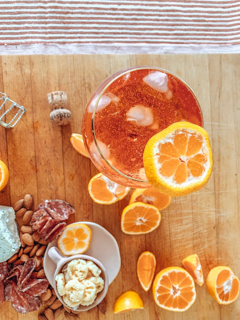 A freshly made aperol sprit on a charcuterie board with meat, nuts, cheese and oranges